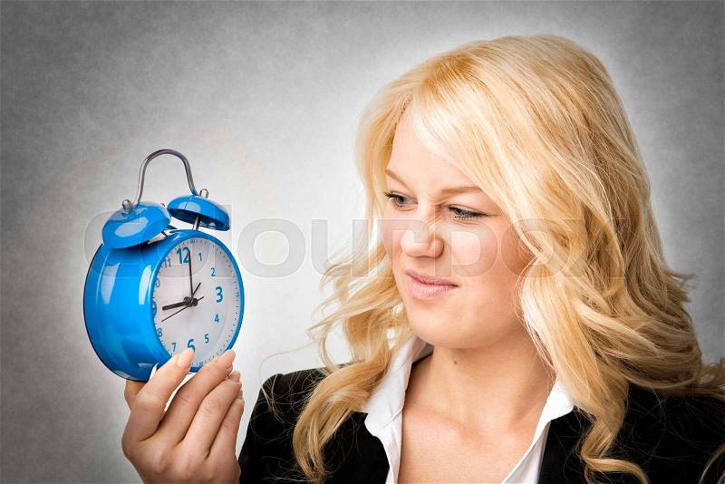Unhappy blond woman unhappy with blue alarm clock, stock photo