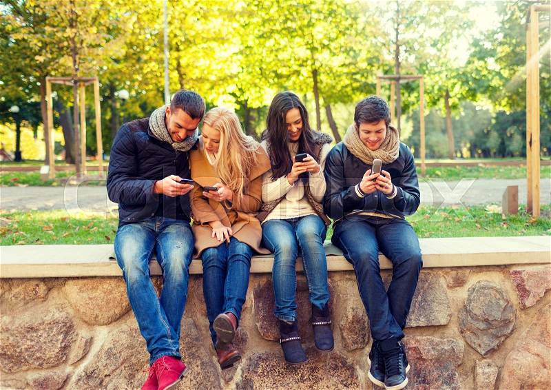Travel, vacation, people, technology and friendship concept - group of smiling friends with smartphones in city park, stock photo