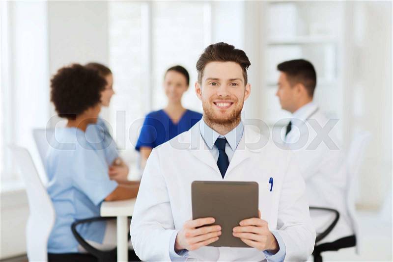Clinic, profession, people and medicine concept - happy male doctor with tablet pc computer over group of medics meeting at hospital, stock photo
