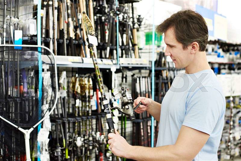 Man chooses fishing rod in the sports shop, stock photo