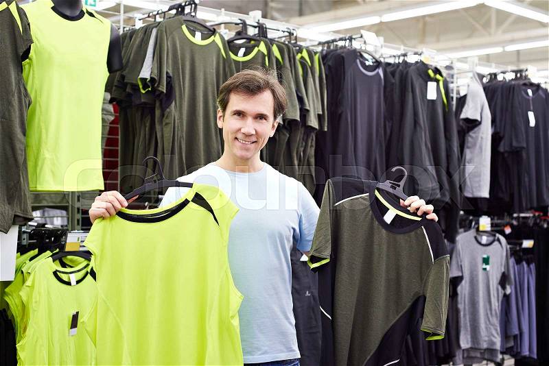 Happy man chooses for t-shirts in sport shop, stock photo
