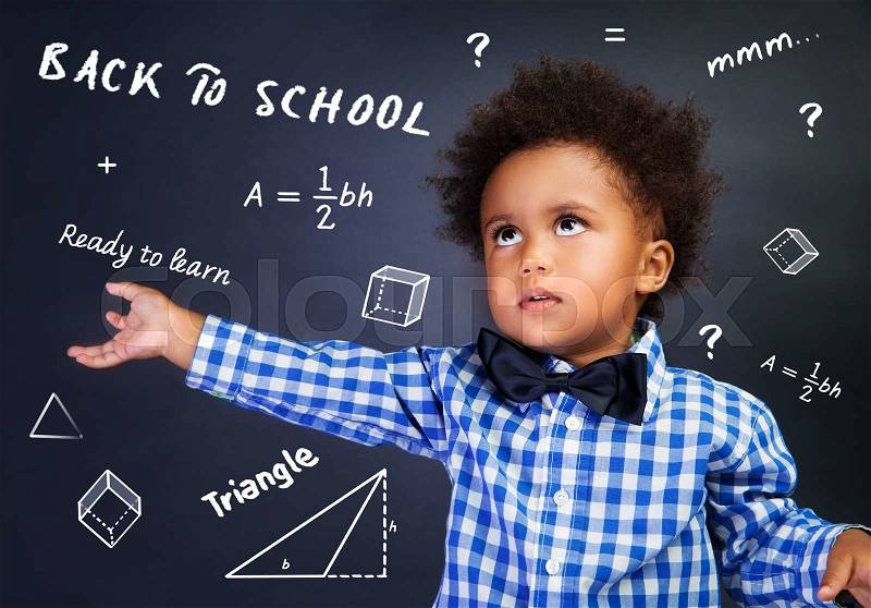 Portrait of smart curly African American schoolboy in the school on mathematics lesson, solving task near blackboard, stock photo