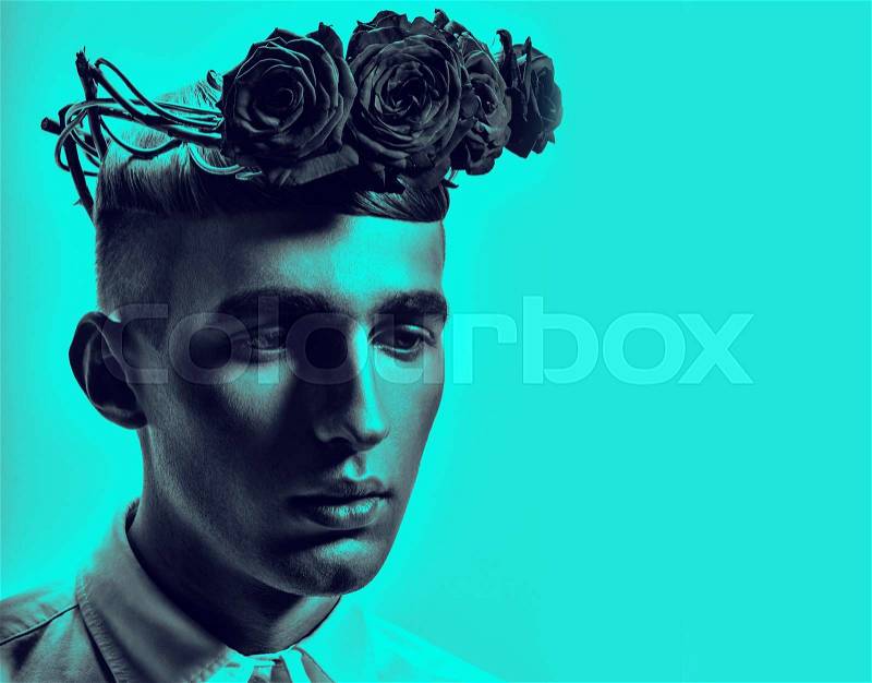 Close up portrait of young handsome man with rose wreath on head.Studio shot.Blue background.Fashion look.Stylish haircut, stock photo