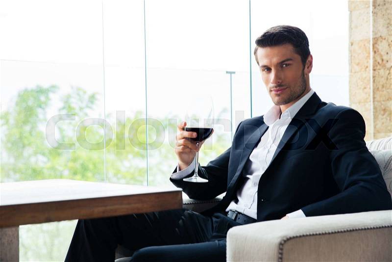 Confident young businessman sitting at restaurant with glass of wine, stock photo