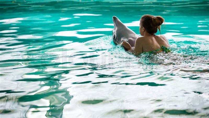 Young woman Swimming with the Dolphin in the Swimming Pool in the Bright Sunny Day, stock photo