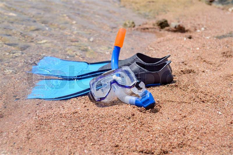 Skin diving equipment standing ready on a beach on the sand at the edge of the sea with a pair of flippers, snorkel and goggles, conceptual of recreational activities on summer vacation, stock photo