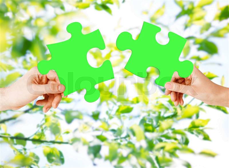 Nature, ecology, energy saving, people and environment concept - close up of couple hands trying to connect green puzzle pieces over natural background, stock photo