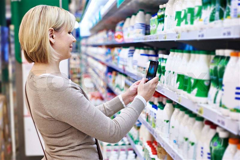 Woman photographing with smartphone label of dairy products in shop, stock photo