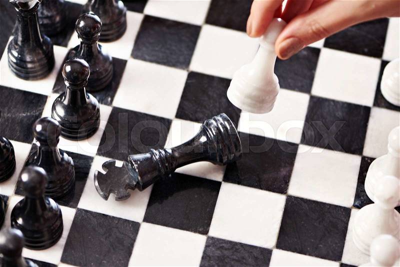Hand with white pawn hits black king closeup, stock photo