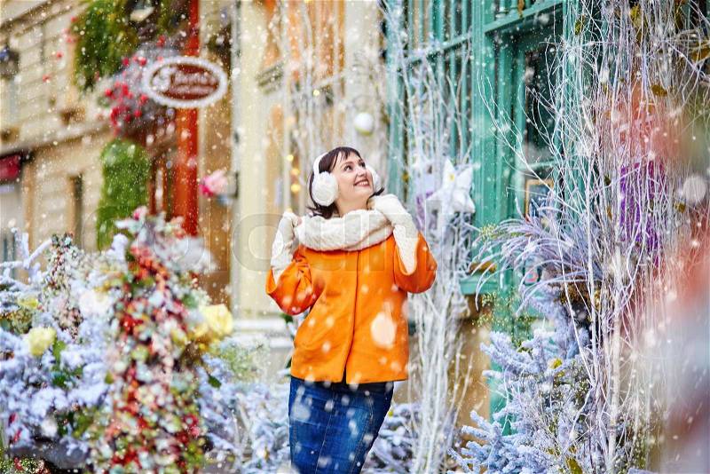 Happy young girl on a Parisian street cafe on winter day during snowfall, stock photo