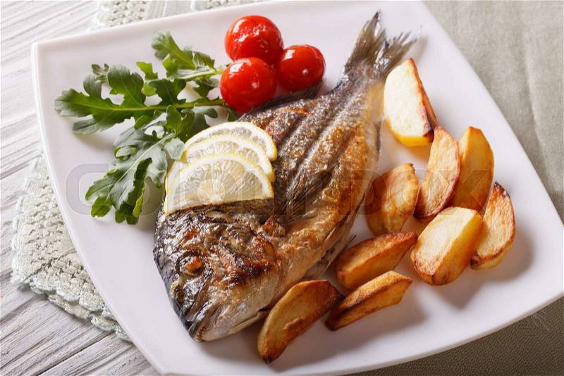Grilled dorado fish with fried potatoes and lemon on a plate close-up. Horizontal , stock photo