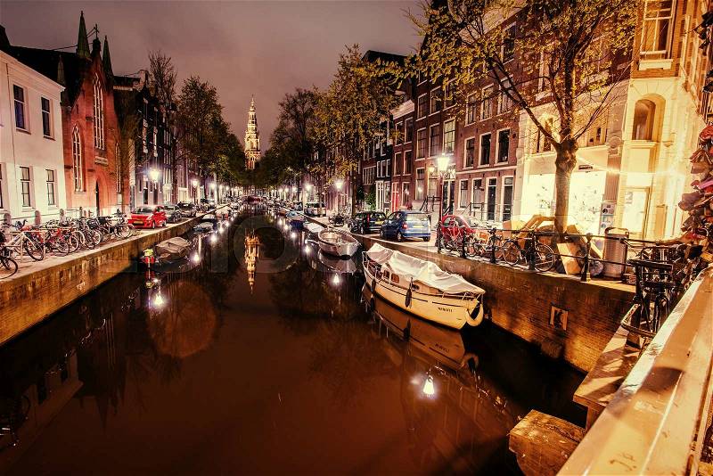 Beautiful night in Amsterdam. Night illumination of buildings and boats near the water in the canal, stock photo