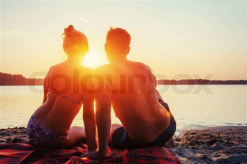 Romantic couple on the beach at colorful sunset on background, stock photo