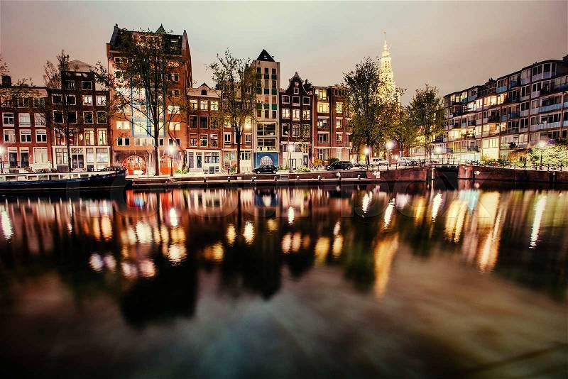 Beautiful night in Amsterdam. Night illumination of buildings and boats near the water in the canal, stock photo