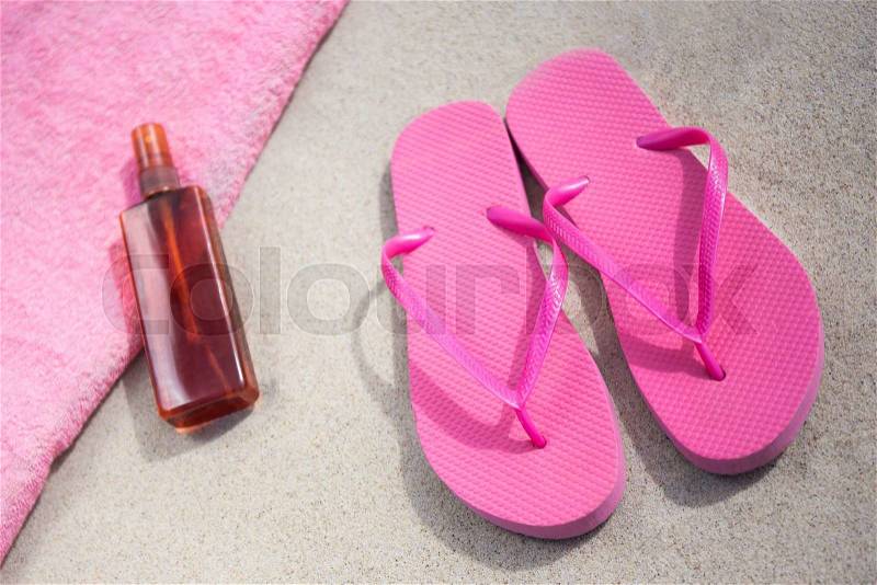 Travel and summer concept - pink flip flops and suntan lotion bottle on sandy beach, stock photo