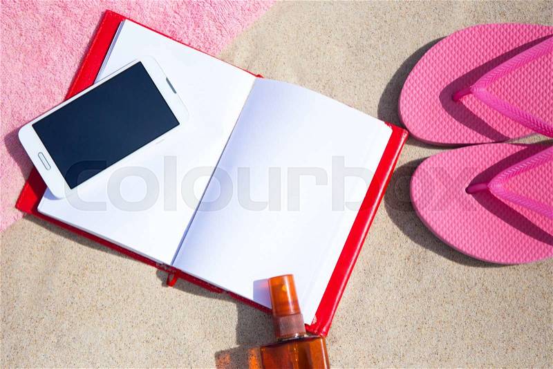 Summer concept - close up of flip flops, towel, phone, book and suntan lotion bottle on sandy beach, stock photo