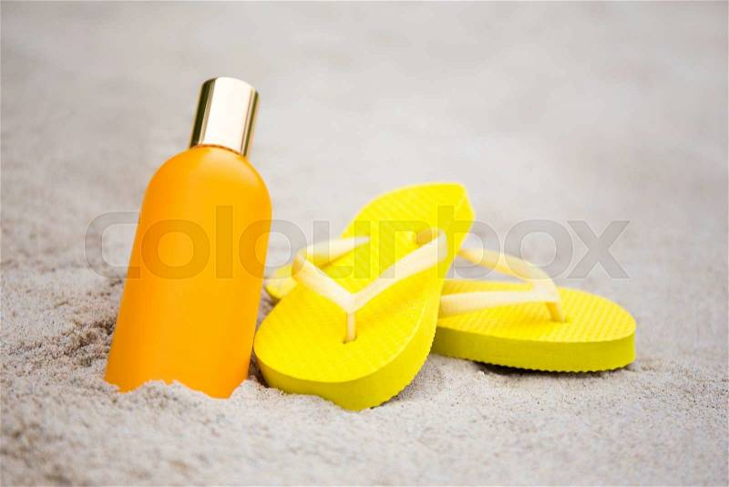 Summer concept - yellow slippers and suntan lotion bottle on sandy beach, stock photo