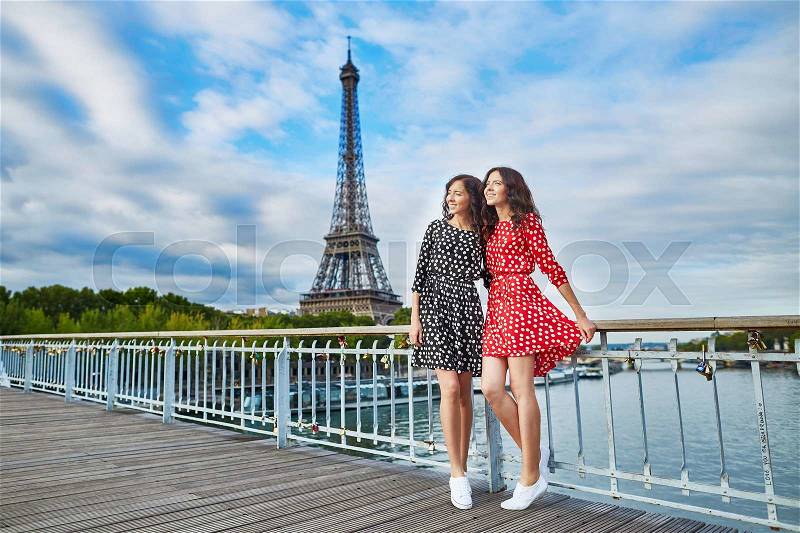 Beautiful twin sisters in red and black polka dot dresses in front of the Eiffel tower in Paris, France, stock photo