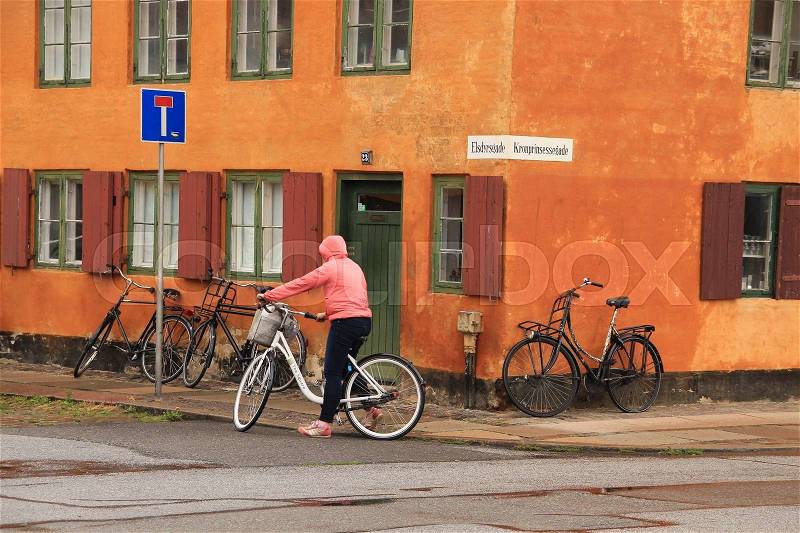 The lady with the pink raincoat stops on the square with the famous painted terraced houses in the capital Copenhagen in Denmark in the wet summer, stock photo