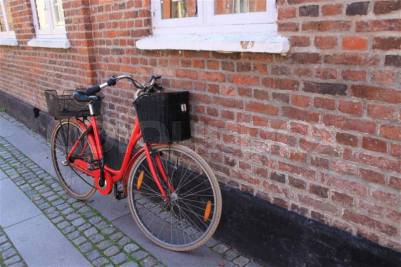 The striking red bike with bicycle basket is standing against the wall of the house in the residential area in the village in the summer, stock photo