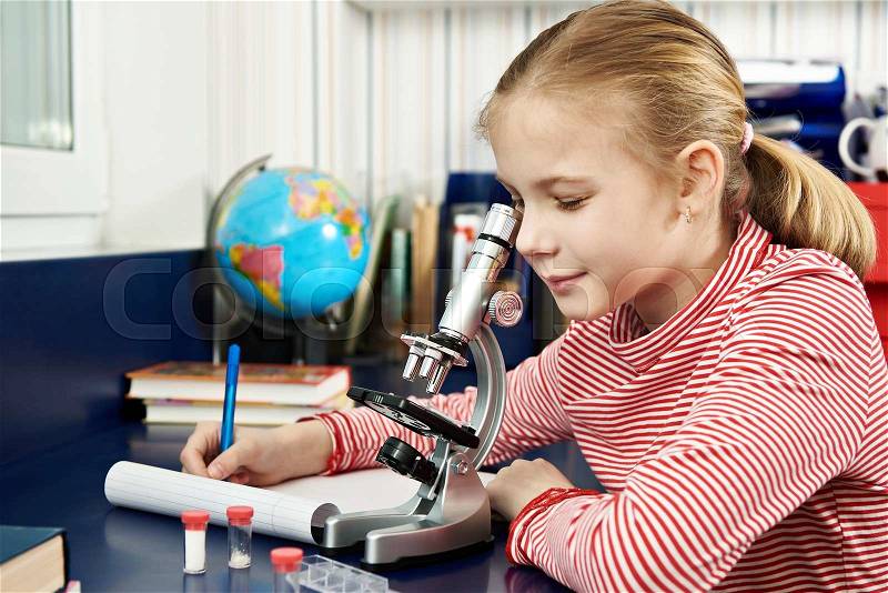 Girl uses a microscope and writes results at home learning table, stock photo