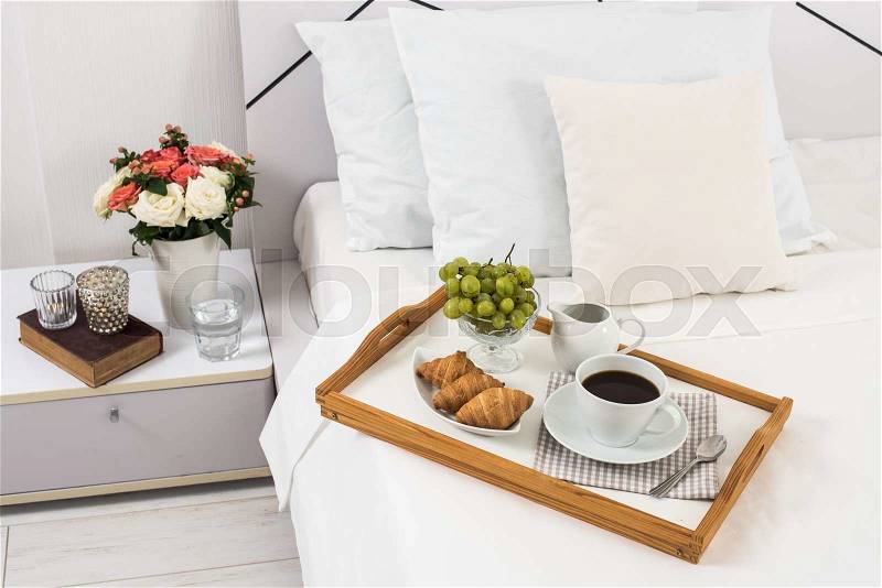 Breakfast in bed, tray with coffee, fruits and croissants on a bed with white linen in bedroom interior, hotel room, stock photo