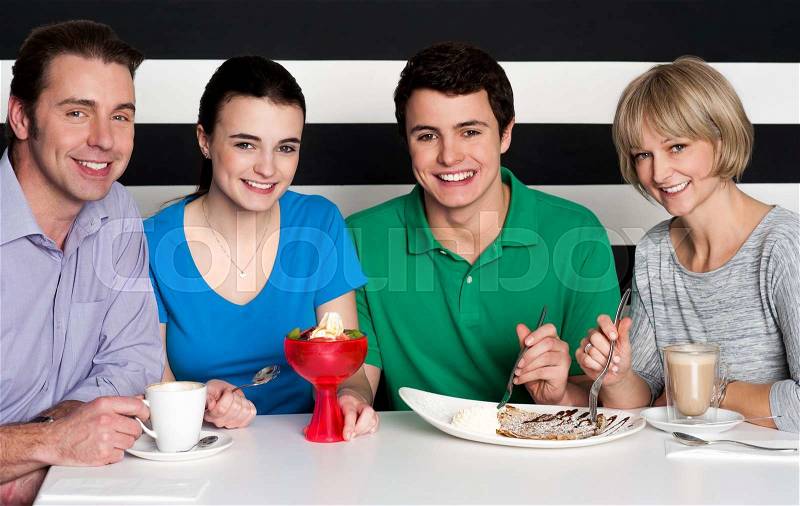 Family of four enjoying breakfast together at restaurant, stock photo