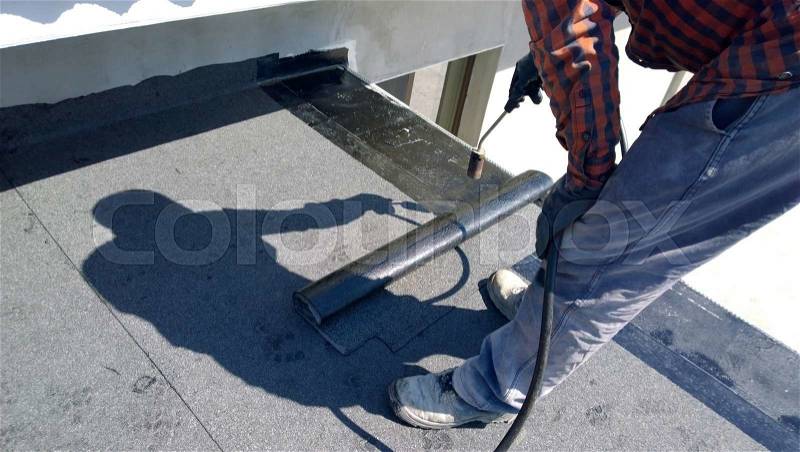 Roofer preparing part of bitumen roofing felt roll for melting by gas heater torch flame, stock photo