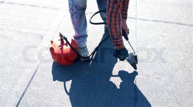 Roofer preparing part of bitumen roofing felt roll for melting by gas heater torch flame, stock photo