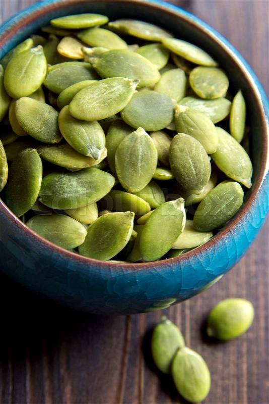 Pumpkin seeds in blue bowl over wooden background close up, stock photo