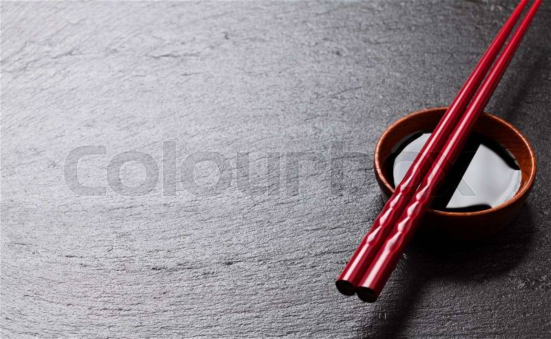 Japanese sushi chopsticks over soy sauce bowl on black stone background. Top view with copy space, stock photo