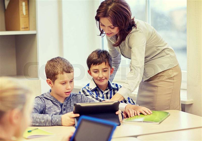 Education, elementary school, learning and people concept - teacher helping school kids with tablet pc computer in classroom, stock photo