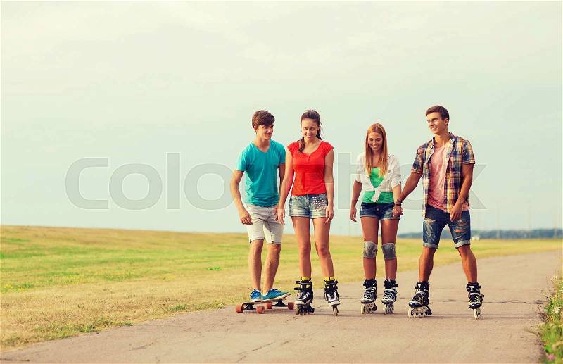 Holidays, vacation, love and friendship concept - group of smiling teenagers with roller skates and skateboard riding outdoors, stock photo