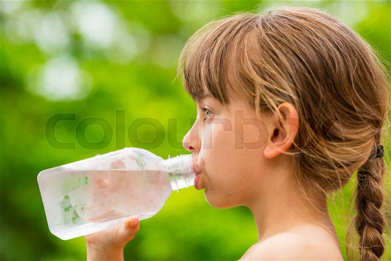 Closeup of young girl drinking pure tap water from transparent plastic drinking bottle while outdoors on a hot summer day, stock photo