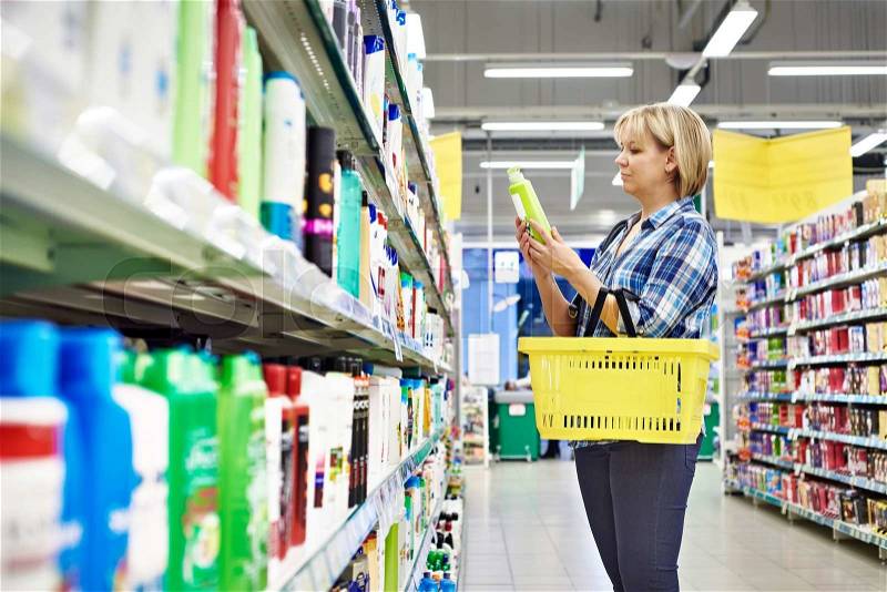Woman chooses shampoo in cosmetics department in supermarket, stock photo