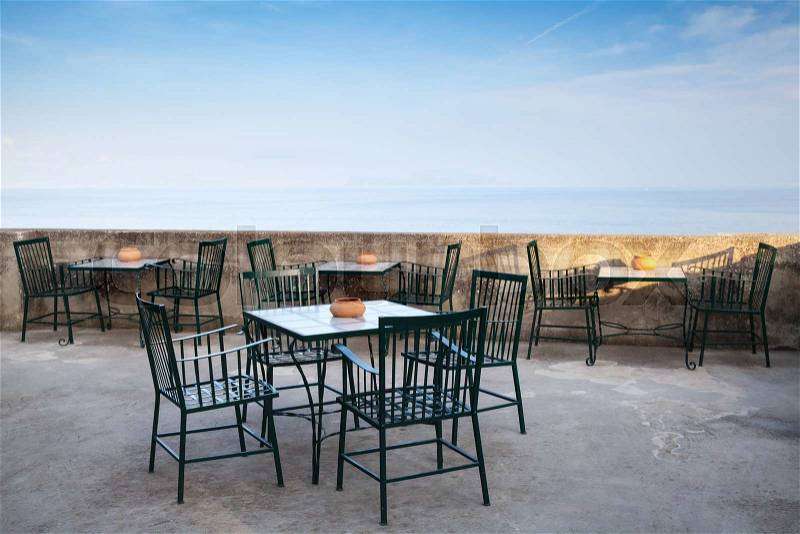 Open space seaside restaurant interior with metal chairs under blue sky, stock photo