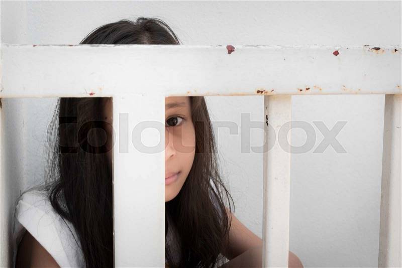 A little girl is hide inside white metal fence, stock photo