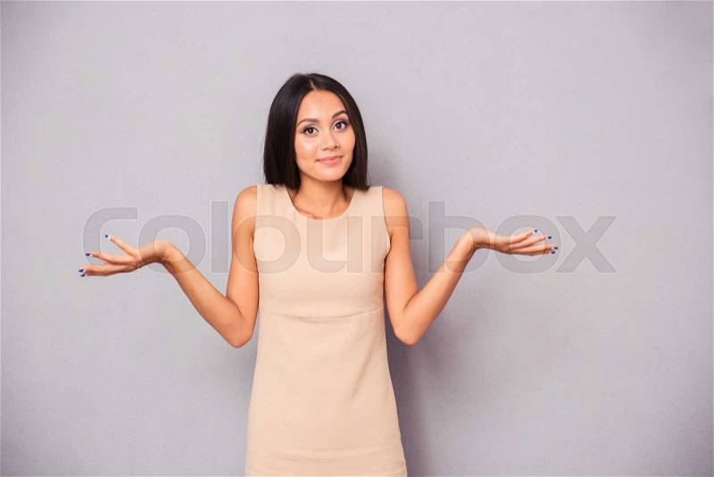 Portrait of a young woman shrugging shoulders over gray background, stock photo