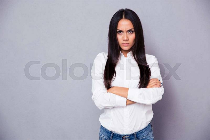 Portrait of angry woman standing with arms folded on gray background, stock photo