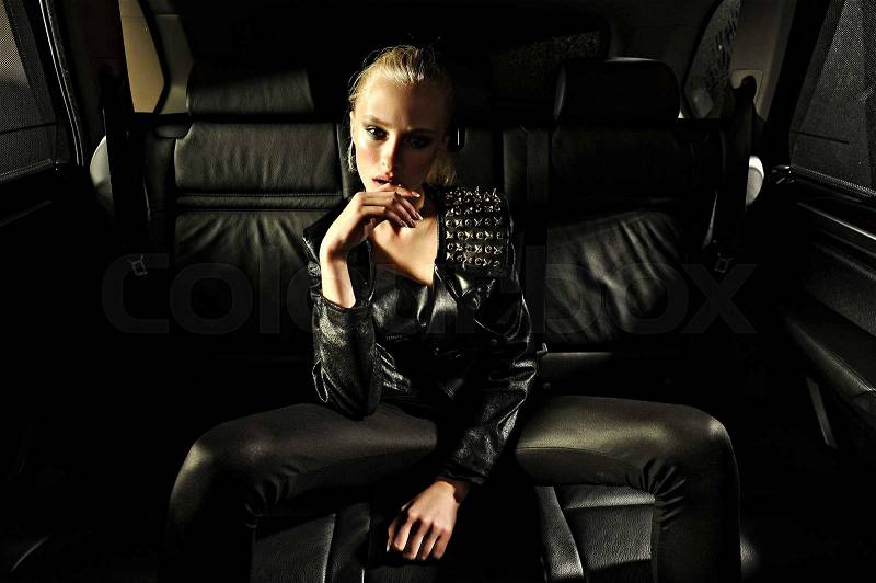 Young blonde woman in black leather jacket,leggings,shoes poses on back seat car.Fashion look.Stylish clothes.Professional make up, stock photo