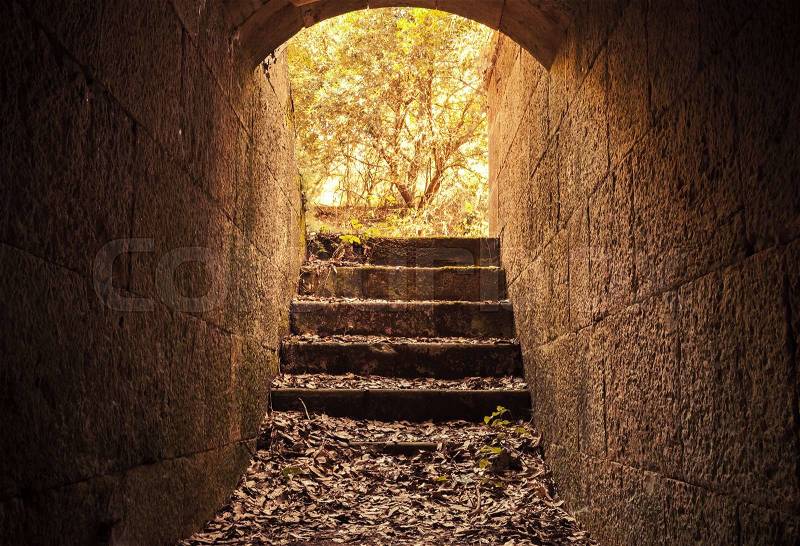 Glowing exit with stairs from dark abandoned concrete tunnel interior, warm tonal correction filter, stock photo