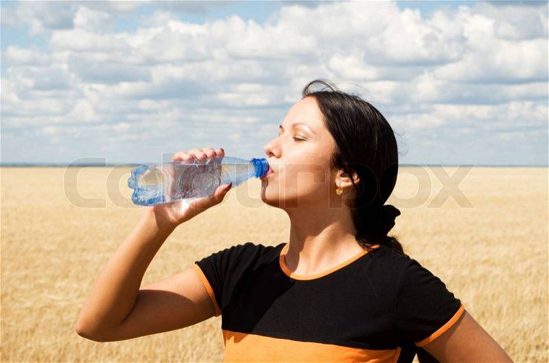 A young beautiful girl drinking water over sky background, stock photo