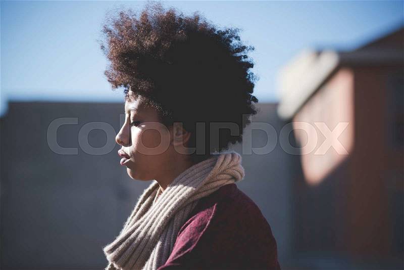 Profile of a young beautiful black curly hair african woman in town, with eyes closed, pensive - youth, pensive, serious concept, stock photo