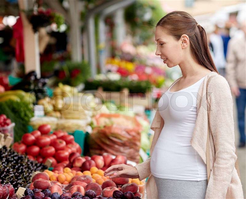 Sale, shopping, pregnancy and people concept - happy pregnant woman choosing food at street market, stock photo
