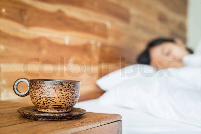 Close up wood coffee cup on table and women on the bed, stock photo
