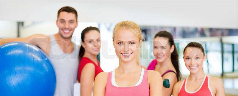 Fitness, sport, training, gym and lifestyle concept - smiling woman standing in front of the group of people in gym, stock photo