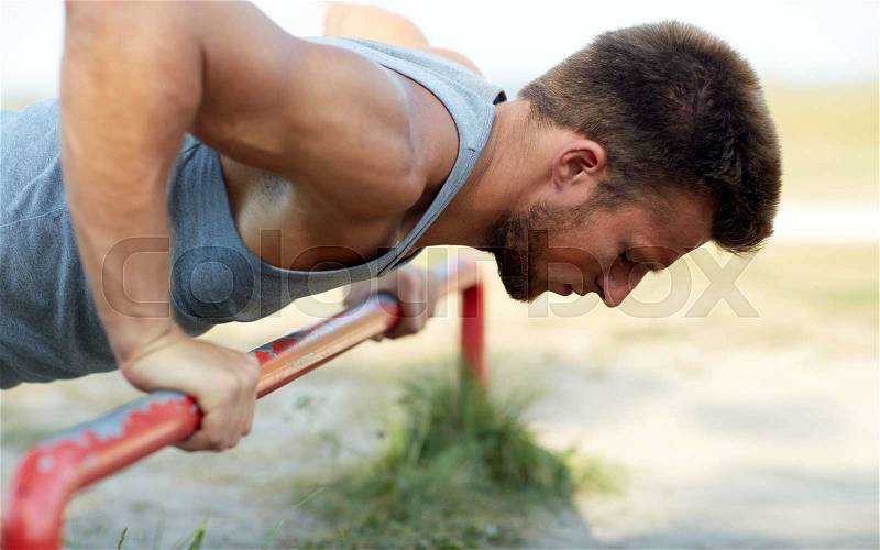 Fitness, sport, exercising, training and lifestyle concept - young man doing push ups on horizontal bar outdoors, stock photo