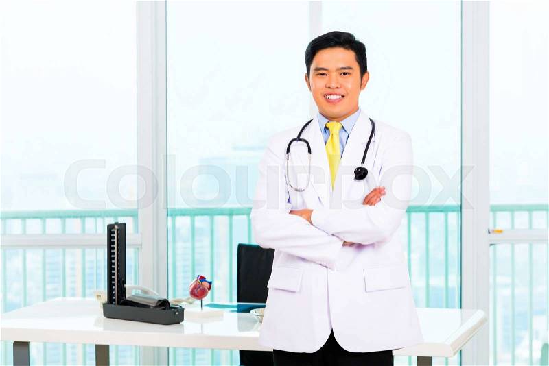 Asian doctor standing proud in his office or medical practice, stock photo