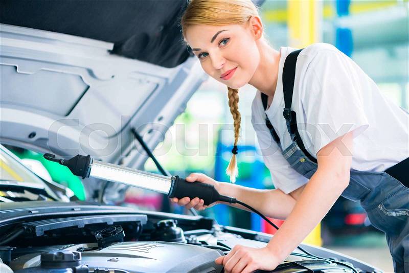 Female mechanic examine car engine with light in workshop , stock photo