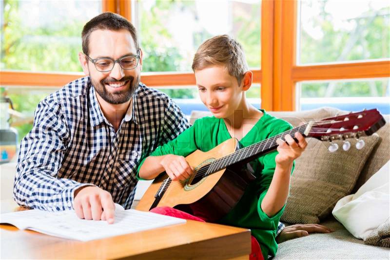 Father and son playing guitar at home, making music together, stock photo
